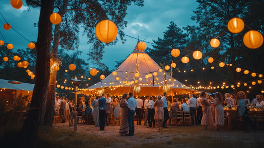 Outdoor wedding reception with hanging orange paper lanterns and tipi marquee at twilight